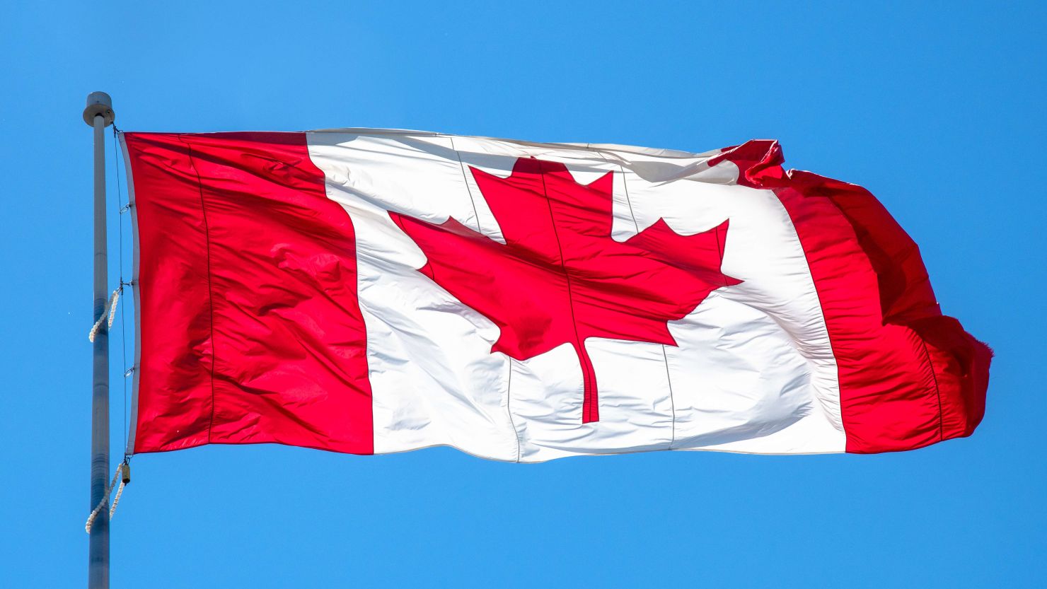 Flag of Canada or Canadian flag waving on blue clear sky.