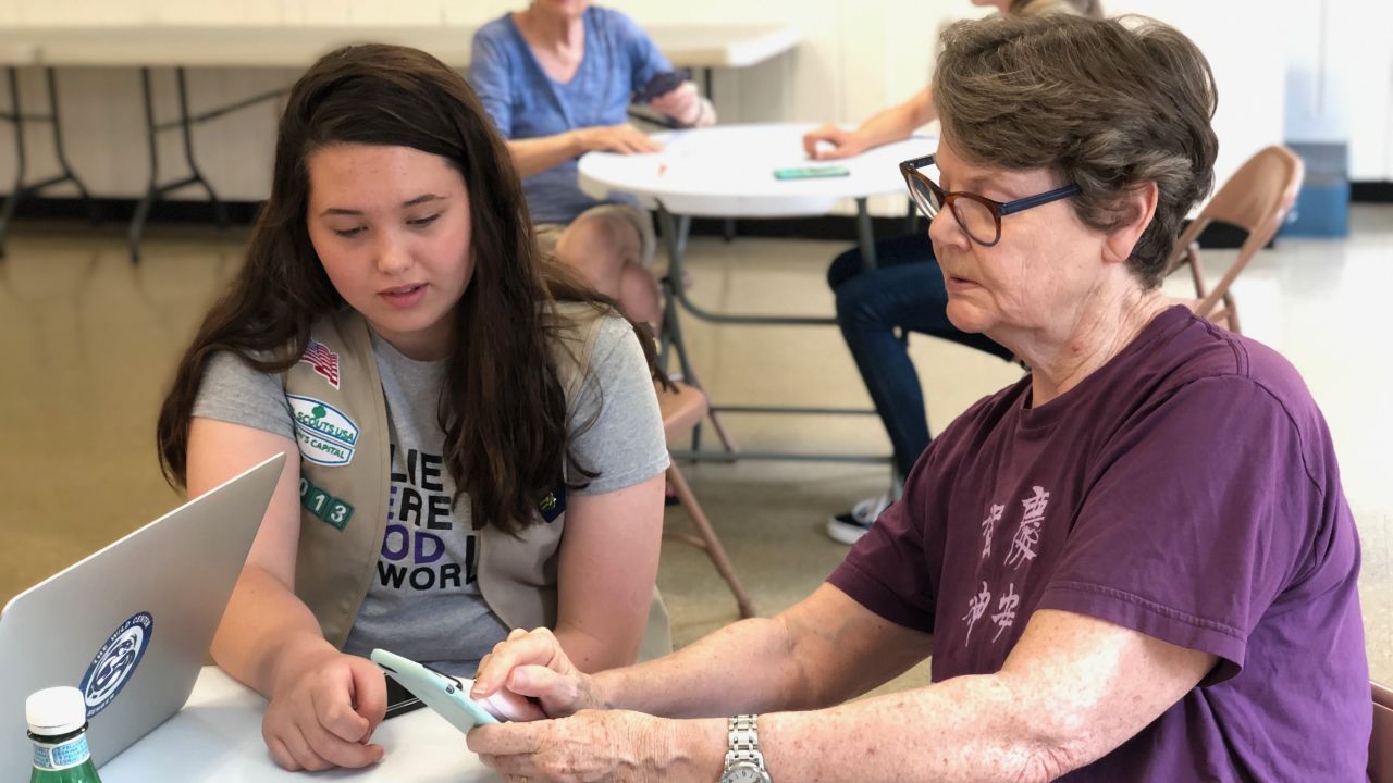 Girl Scout Cadette Maura Sammis (left) helps an attendee at a smartphone clinic for senior citizens.