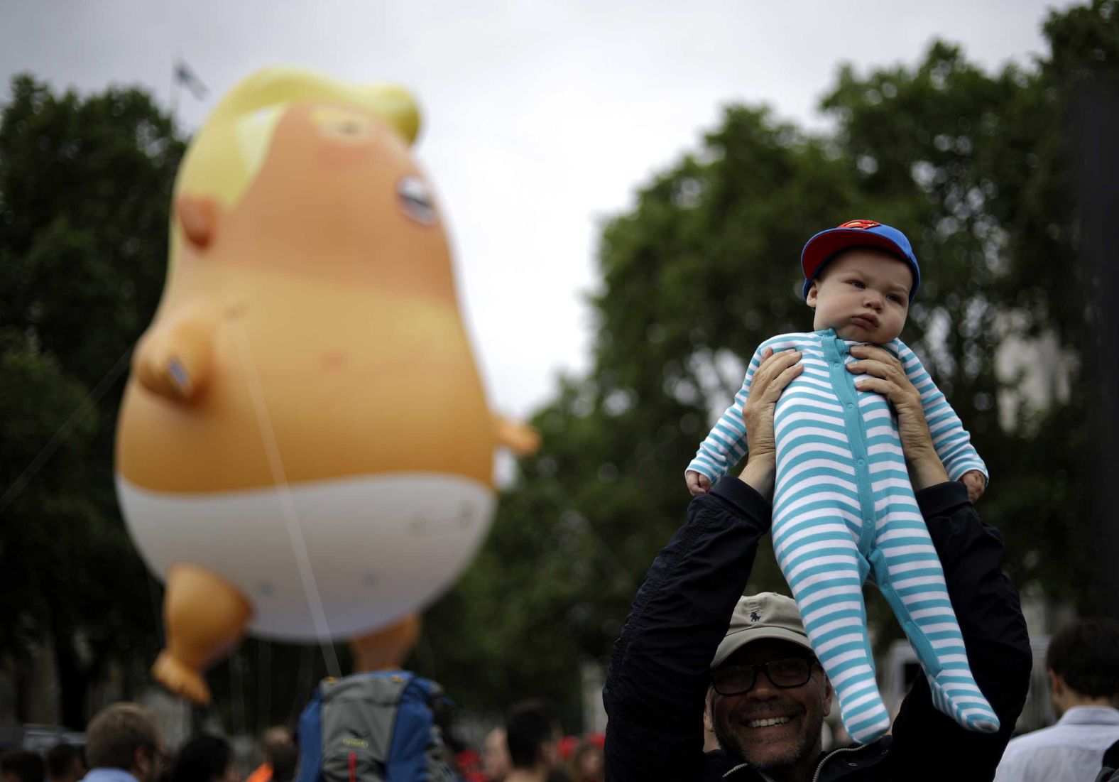 A man lifts up a baby near the "Trump Baby" blimp as people start to gather for protests in Parliament Square.