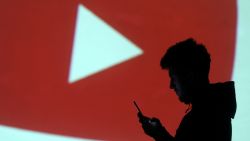 A silhouette of a mobile user is seen next to a screen projection of Youtube logo in this picture illustration taken March 28, 2018.  REUTERS/Dado Ruvic/Illustration