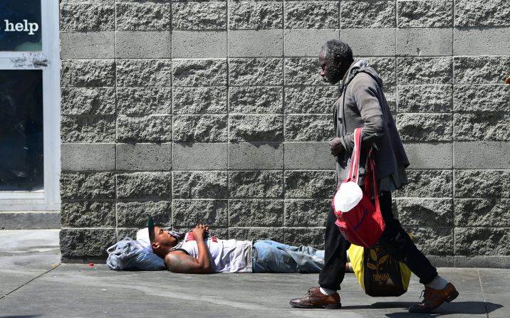 A pedestrian walks past a man sleeping on a sidewalk in Los Angeles on May 30.