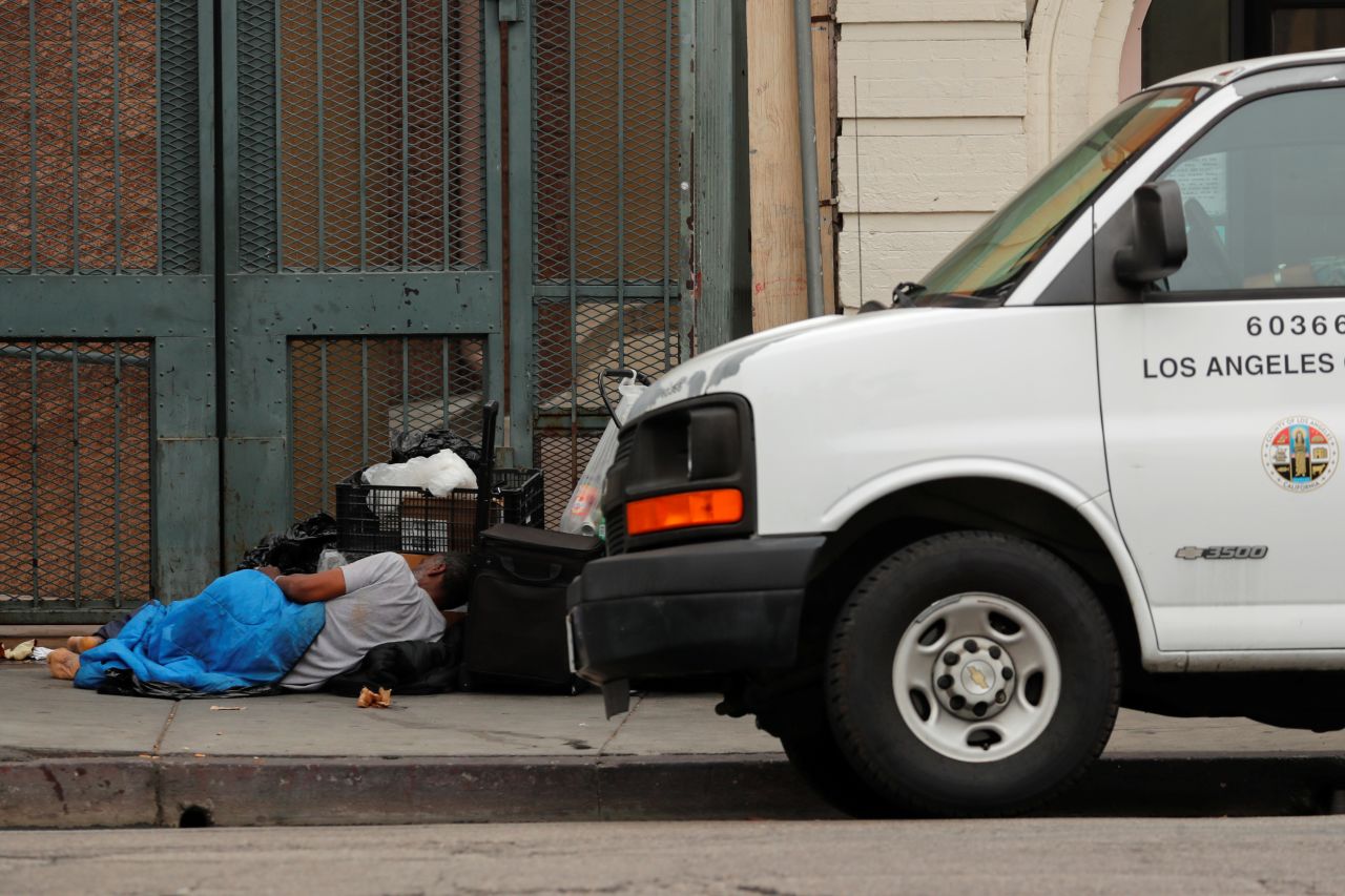 A homeless person sleeps on the sidewalk next to a Los Angeles County vehicle on June 4.