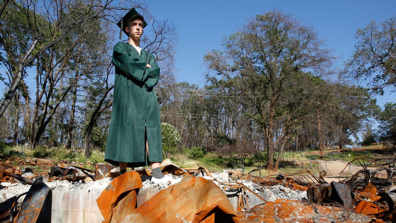 Sean Newsom, a senior at Paradise High School, poses in his cap and gown at the burned ruins of his home.