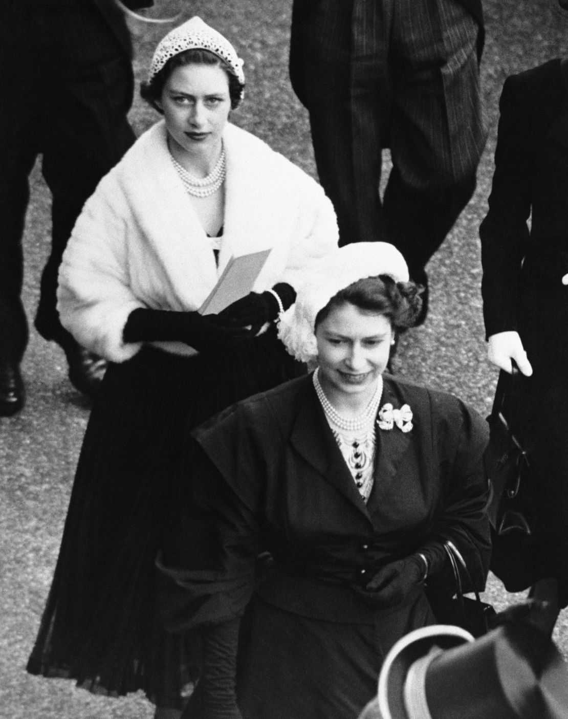 Queen Elizabeth II, dressed in black with a white hat, followed by Princess Margaret at the the second day of Royal Ascot in 1952. 