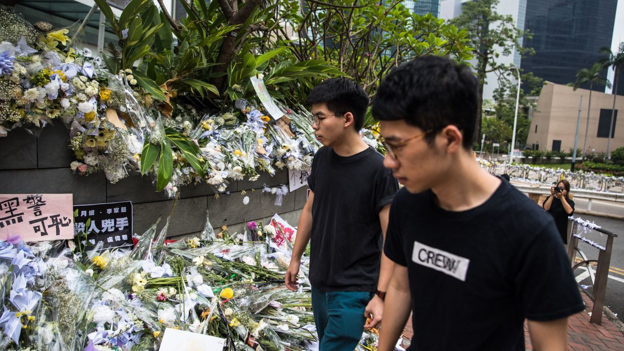 Hong Kong pro-democracy activist Joshua Wong (left), who was just released from jail, walks past flower tributes at a makeshift memorial site for a protester who fell to his death while hanging banners against a controversial extradition law proposal on June 15, in Hong Kong on June 17, 2019.