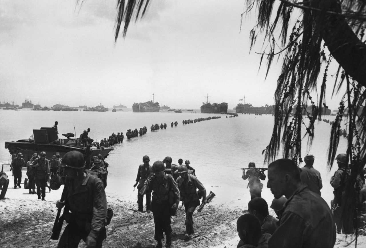 Army reinforcements wade ashore on Saipan without enemy opposition. They relieved Marines in the battle of attrition raging in the island's interior. The ships of Task Force 58 are behind them in the Pacific Ocean.