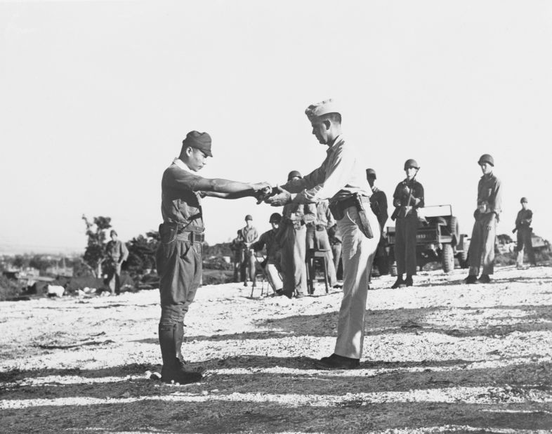 Imperial Japanese Army Capt. Sakae Oba surrenders his sword to Lt. Col. Howard C. Kurgis.