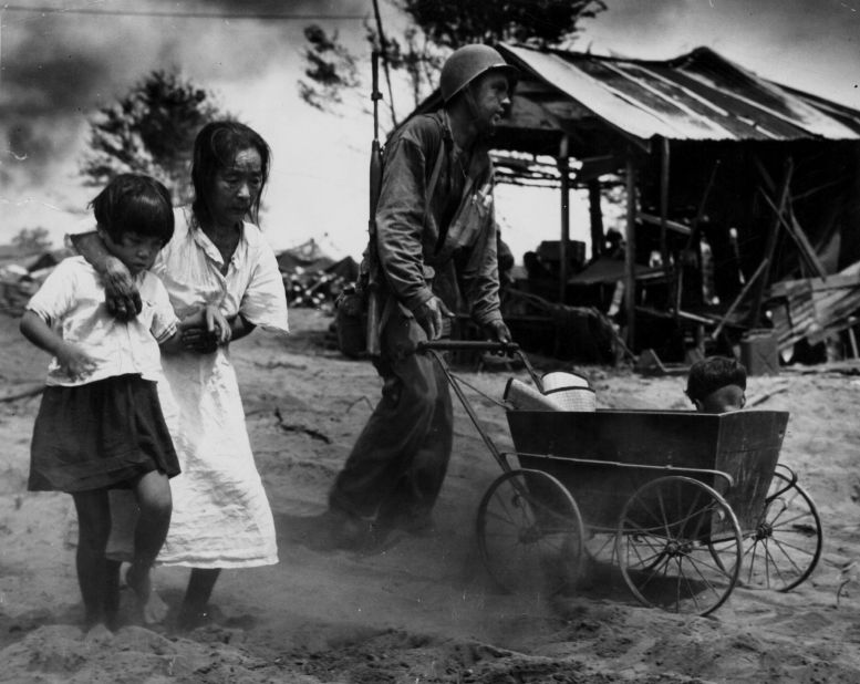 A US soldier pushes a baby carriage while escorting a family to an internment camp during the Battle of Saipan.