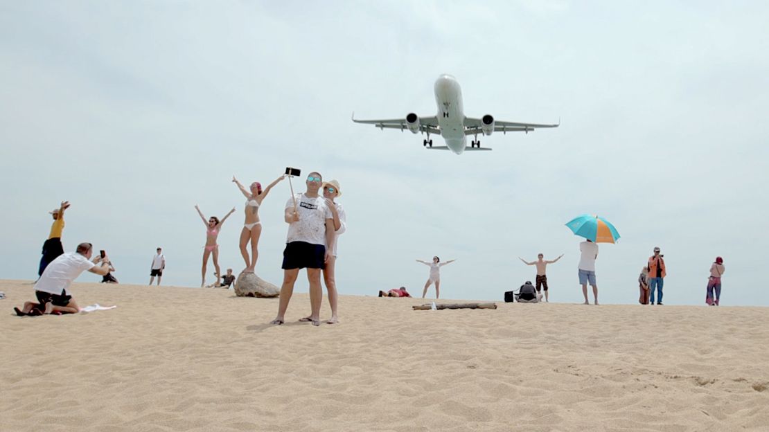 Tourists pose for photographs as an airplane descends into Phuket International Airport in 2019. The airport is currently closed to all commercial flights due to the coronavirus outbreak.   