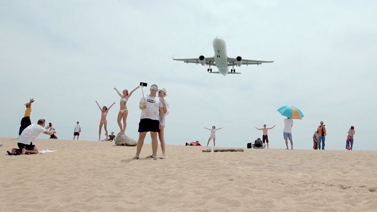 Tourists pose for photographs as an airplane descends into Phuket International Airport in 2019. The airport is currently closed to all commercial flights due to the coronavirus outbreak.