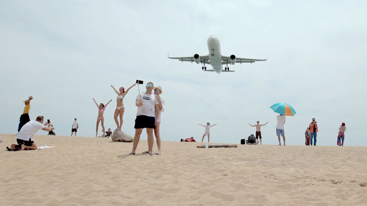 Tourists pose for photographs as an airplane descends into Phuket International Airport.