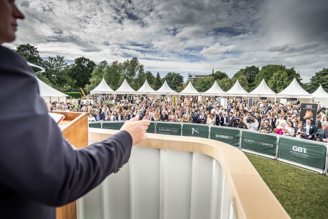 An auctioneer encourages guests to bid amid a garden party atmosphere.