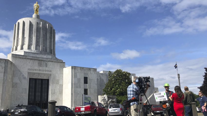 A TV reporter interviews self-employed logger Bridger Hasbrouck, of Dallas, Ore., outside the Oregon State House in Salem, Ore., on Thursday, June 20, 2019, the day the Senate is scheduled to take up a bill that would create the nation's second cap-and-trade program to curb carbon emissions. Senate Republicans, however, pledged to walk out so there wouldn't be enough lawmakers present for a vote on House Bill 2020, which is extremely unpopular among loggers, truckers and many rural voters. (AP Photo/Gillian Flaccus)