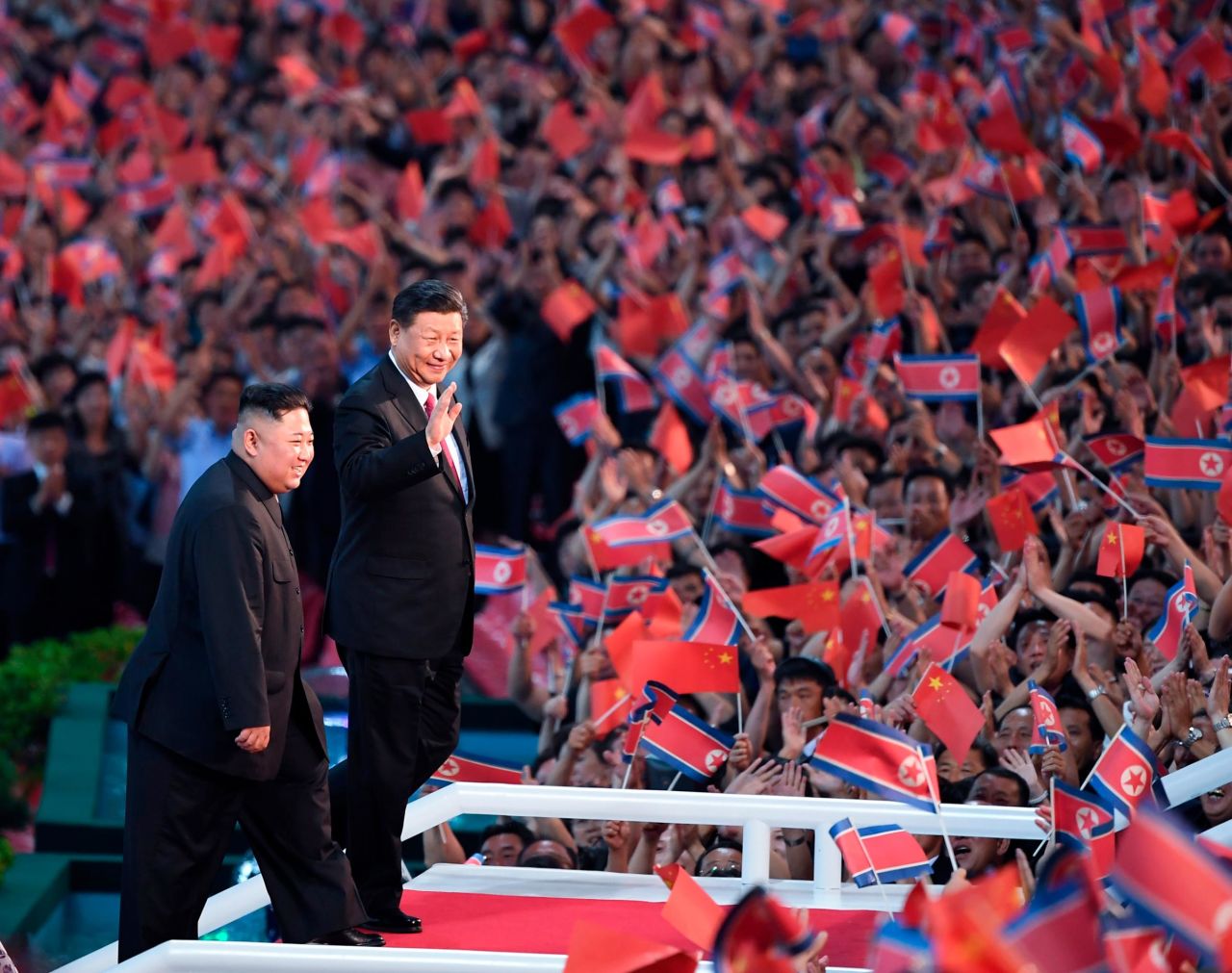 Spectators wave Chinese and North Korean flags as Kim, left, Xi, attend the gymnastic performance at the May Day Stadium.