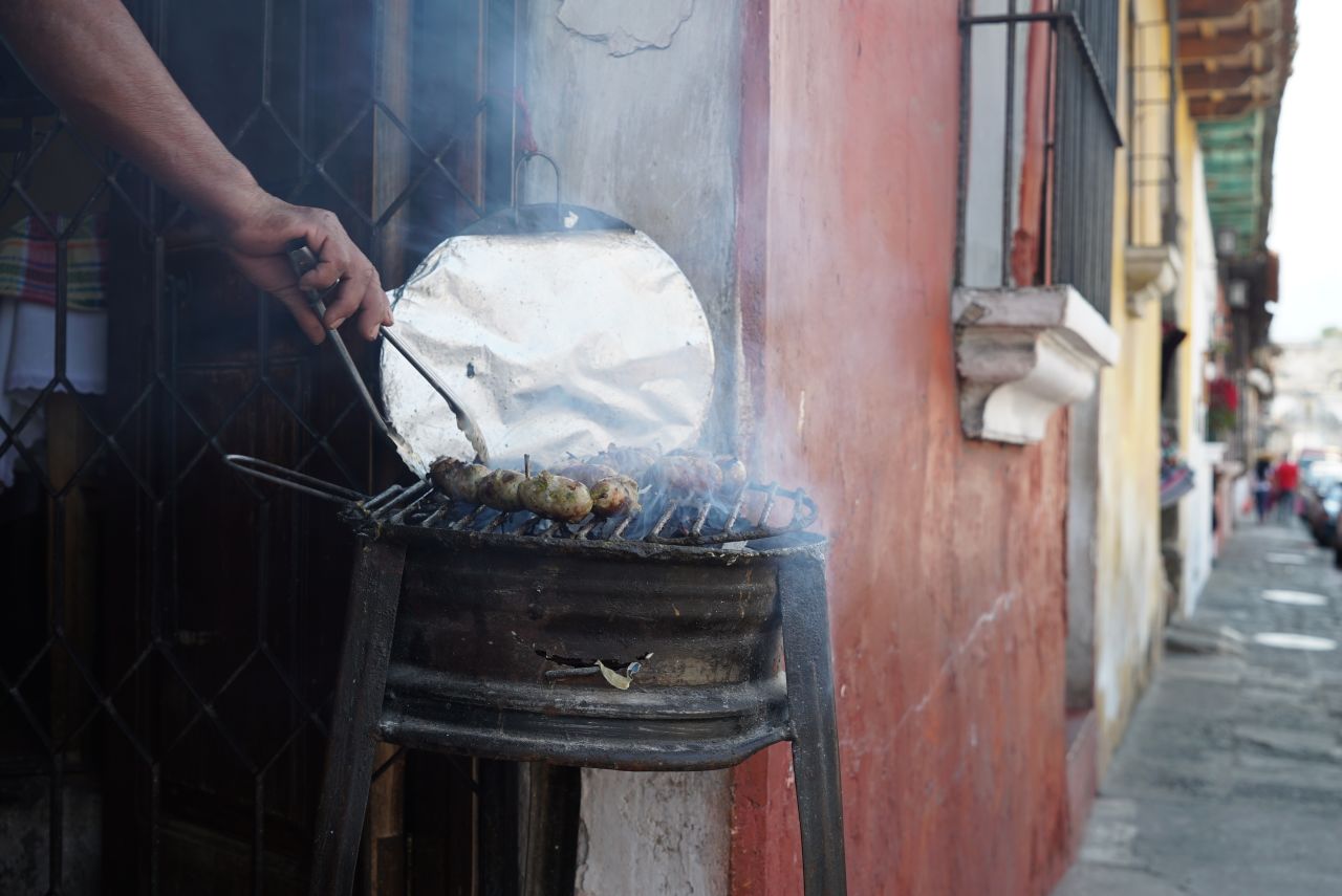 <strong>Sizzling meat:</strong> A shop owner checks on his chorizo as it grills on one of Antigua's cobbled street corners.