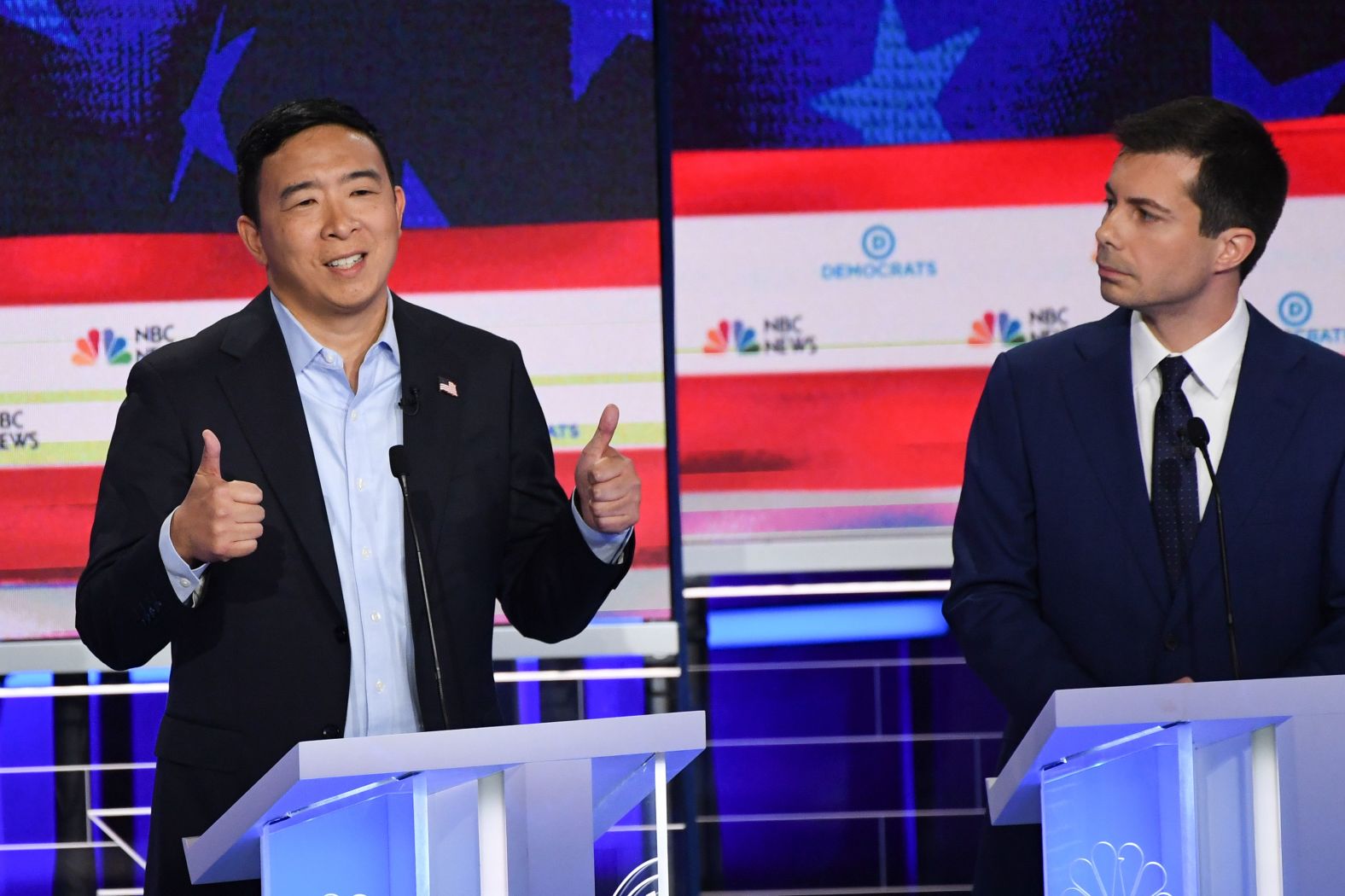 Yang answers a question while Buttigieg looks on. <a href="index.php?page=&url=https%3A%2F%2Fwww.cnn.com%2Fpolitics%2Flive-news%2Fdemocratic-debate-june-27-2019%2Fh_cc7dd7dbb0234b00abcea7f0d23e956a" target="_blank">Yang's platform</a> includes a plan for universal basic income. He wants to give all Americans over the age of 18 $1,000 per month to address economic inequality. He argues the policy would play a key role in restructuring the modern economy to make it more equitable.