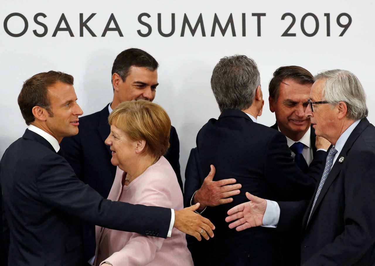 French President Emmanuel Macron reaches out to shake hands on Saturday, June 29, with European Commission President Jean-Claude Juncker, next to Spanish Prime Minister Pedro Sanchez and Germany's Chancellor, Angela Merkel, at the G20 summit.