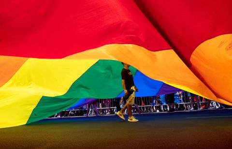 A participant walks under a large rainbow flag.