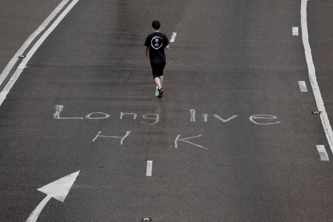A protester wearing a T-shirt with the word "revolution" walks past an inscription on a road that reads "Long Live HK."