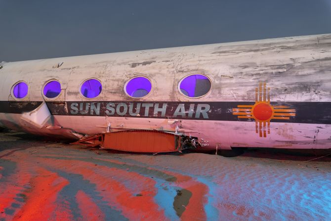 An old movie prop plane lit up in shades of red and purple.