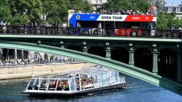 Tourists enjoy a ride on a tourist river boat (Bateaux-Mouche)and tourism bus on the Seine river on a sunny day in Paris on May 6, 2018. (Photo by GERARD JULIEN / AFP)        (Photo credit should read GERARD JULIEN/AFP/Getty Images)