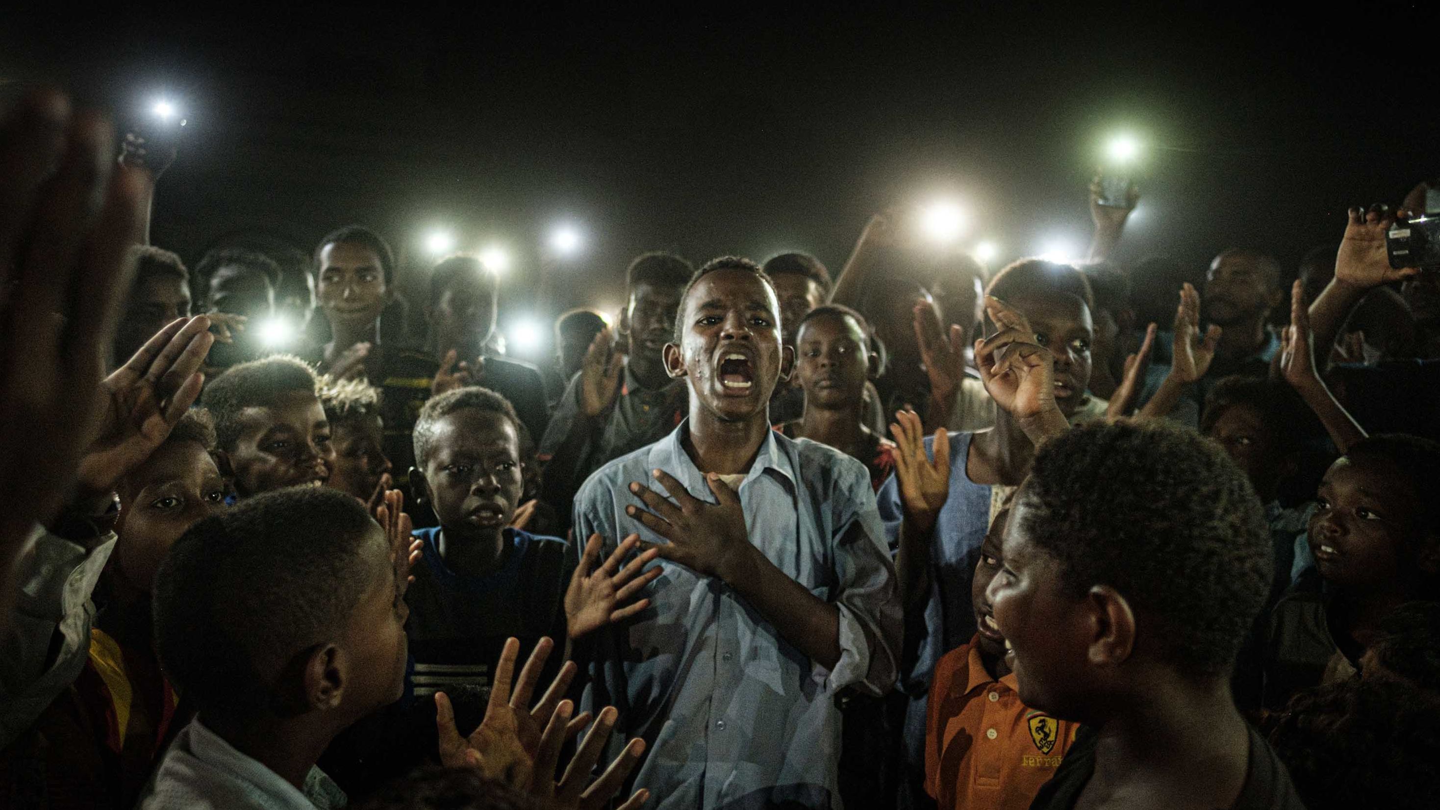 People chant slogans as a young man recites a poem, illuminated by mobile phones on June 19.