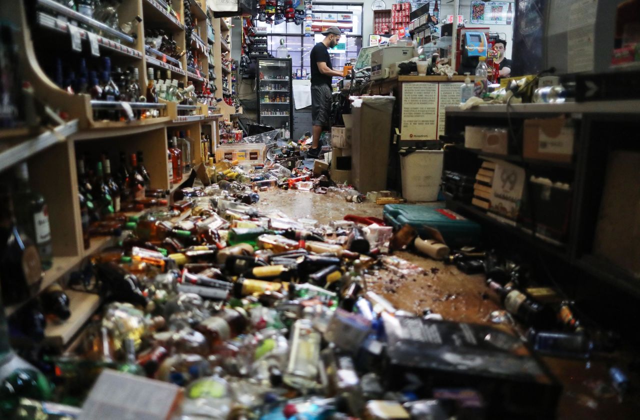 An employee works at the cash register on July 6 at Eastridge Market, near broken bottles scattered on the floor, following a 7.1 magnitude earthquake which struck in the area July 5. 