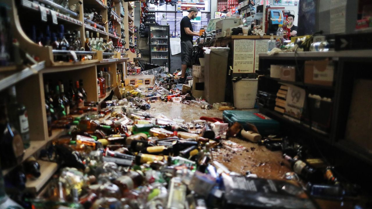 An employee works at the cash register at Eastridge Market, near broken bottles scattered on the floor, following a 7.1 magnitude earthquake, on July 6 in Ridgecrest, California.