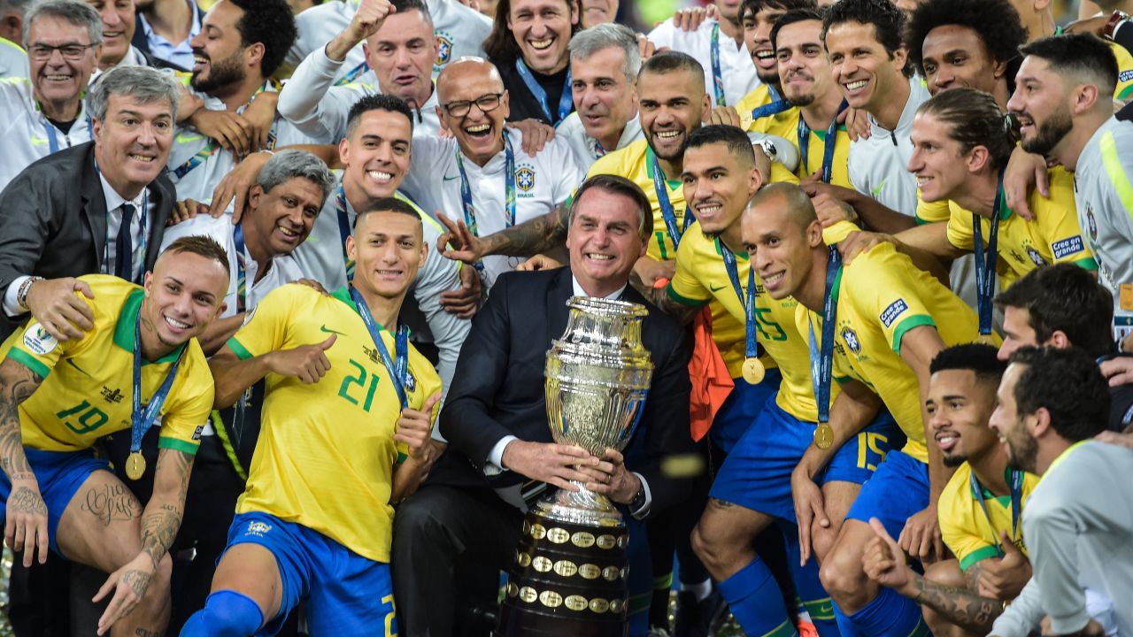 Brazilian President Jair Bolsonaro holds the Copa America trophy as members of the national team celebrate.