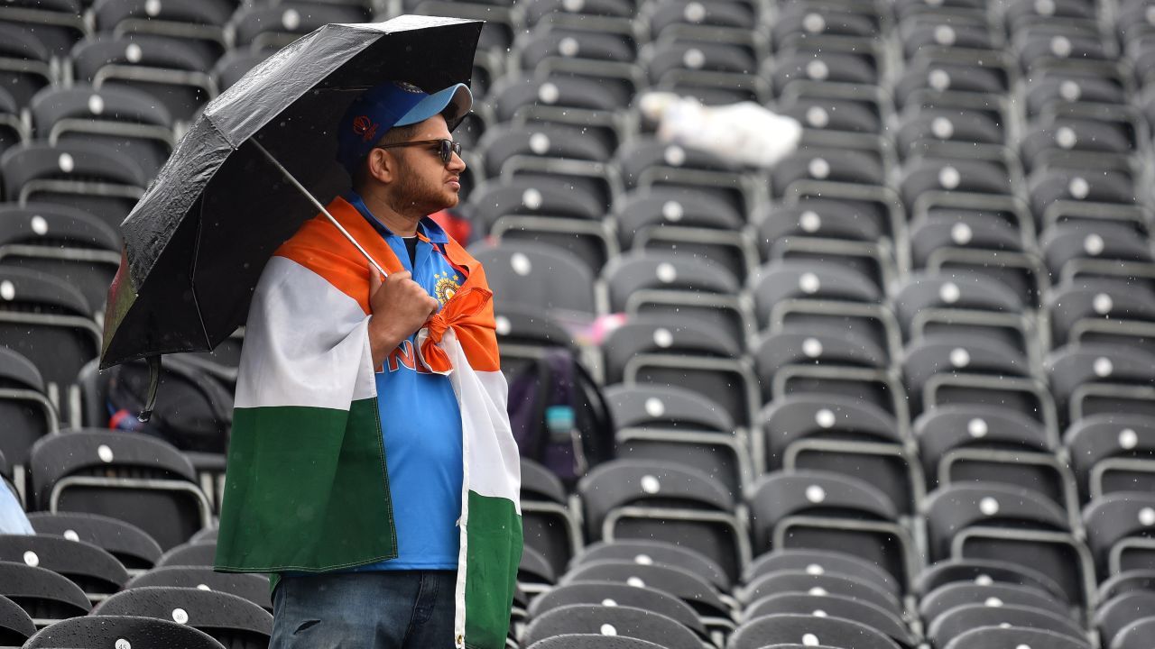 MANCHESTER, ENGLAND - JULY 09:  A fan shelters from the rain as play is delayed during the Semi-Final match of the ICC Cricket World Cup 2019 between India and New Zealand at Old Trafford on July 09, 2019 in Manchester, England. (Photo by Nathan Stirk/Getty Images)