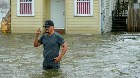 Barry Williams talks to a friend on his smartphone on Saturday, July 13, as he wades through storm surge from Lake Pontchartrain in Mandeville, Louisiana.  