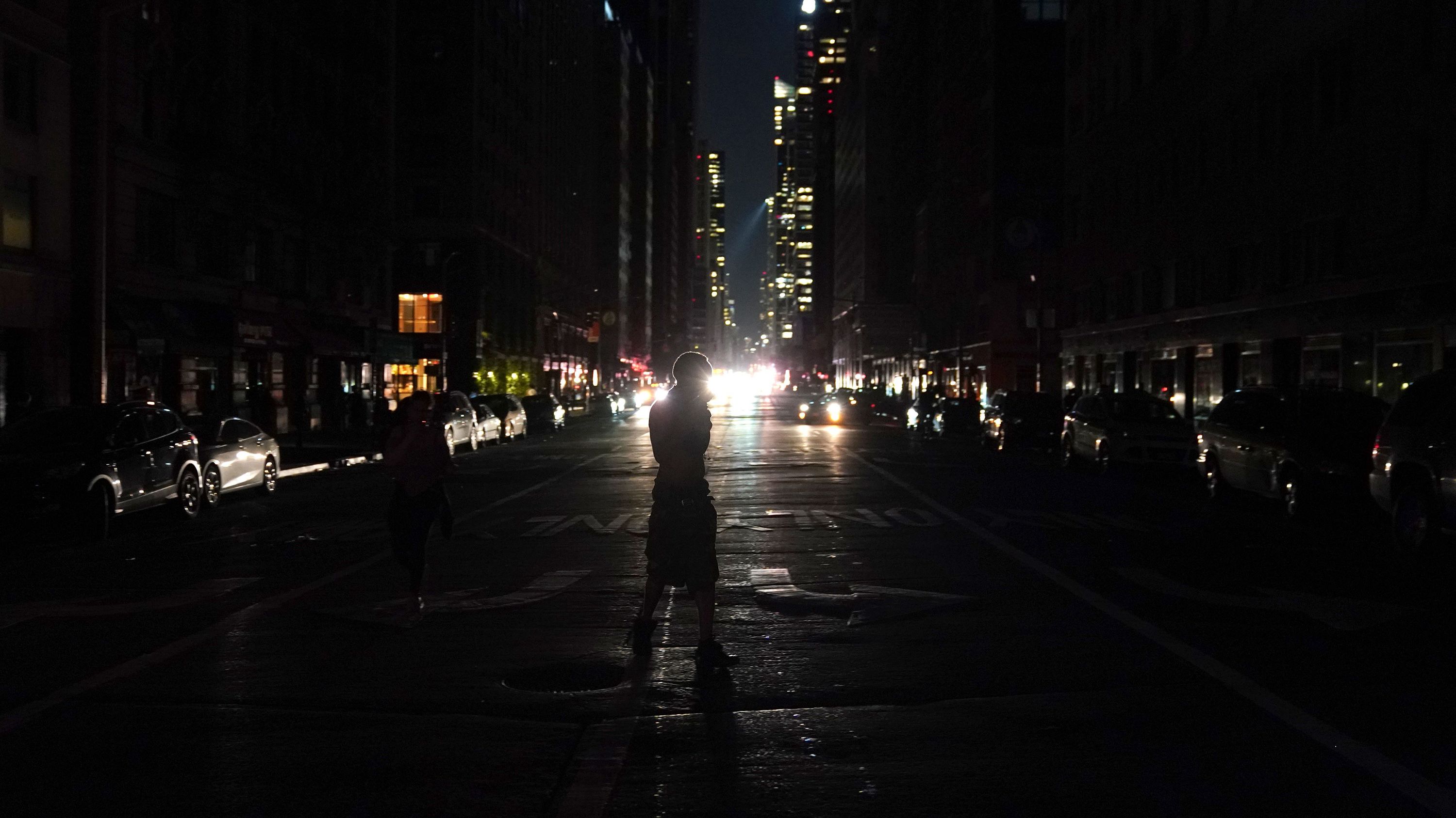 People walk down the streets during a power outage affecting parts of New York City on July 13.