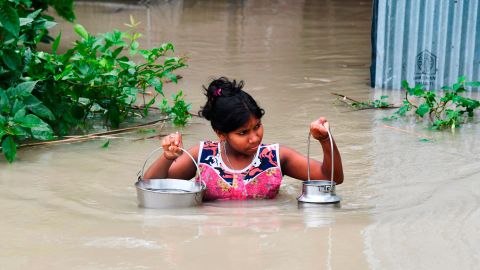 An Indian girl carries drinking water as she wades through flood waters in India's Assam state on July 15, 2019.