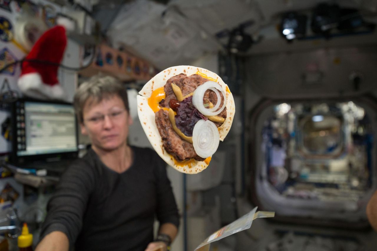 Astronaut Peggy Whitson and her cheeseburger wrapped in a tortilla are shown on the International Space Station. Since the mid '80s, flour tortillas have been a staple bread item in space that provides an almost crumble-free solution.