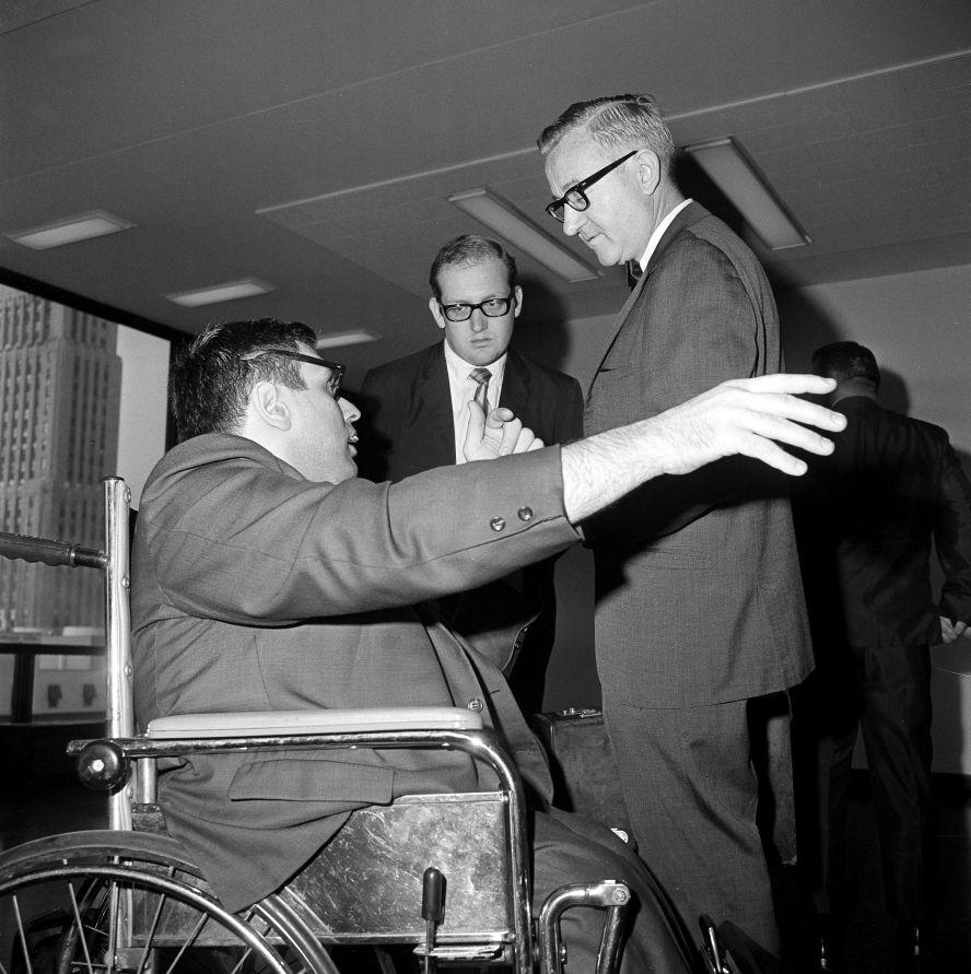 From his wheelchair in a corridor outside a hearing room, Sherman Skolnick engages in discussion with counsel for the commission investigating charges of misconduct against two Supreme Court justices on July 21, 1969, in Chicago. From left, Skolnick, William McNally, assistant and John Paul Stevens, counsel. A witness appearance was under discussion.