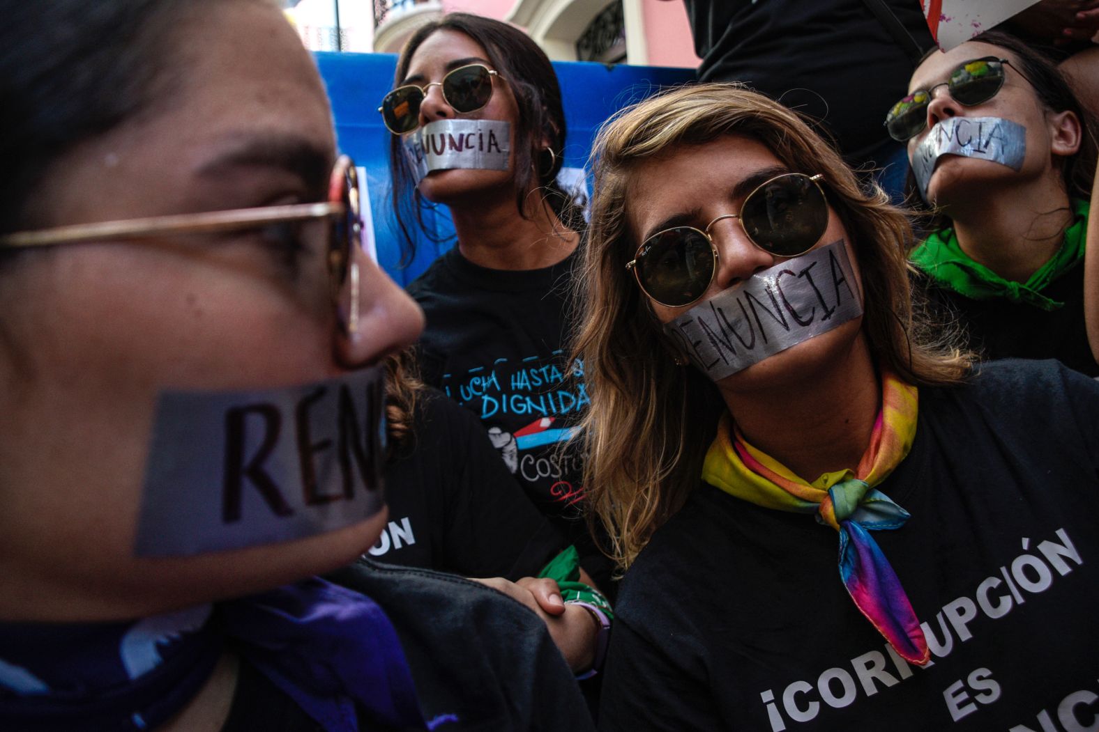 Demonstrators cover their mouths with duct tape that says "resignation" in Spanish.