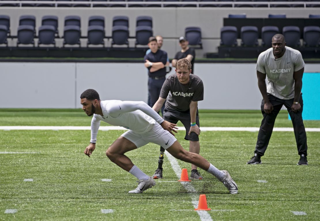 A teen performs in the NFL Academy's trials, watched by British NFL player Efe Obada (right). 
