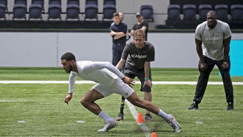 A teen performs in the NFL Academy's trials, watched by British NFL player Efe Obada (right). 
