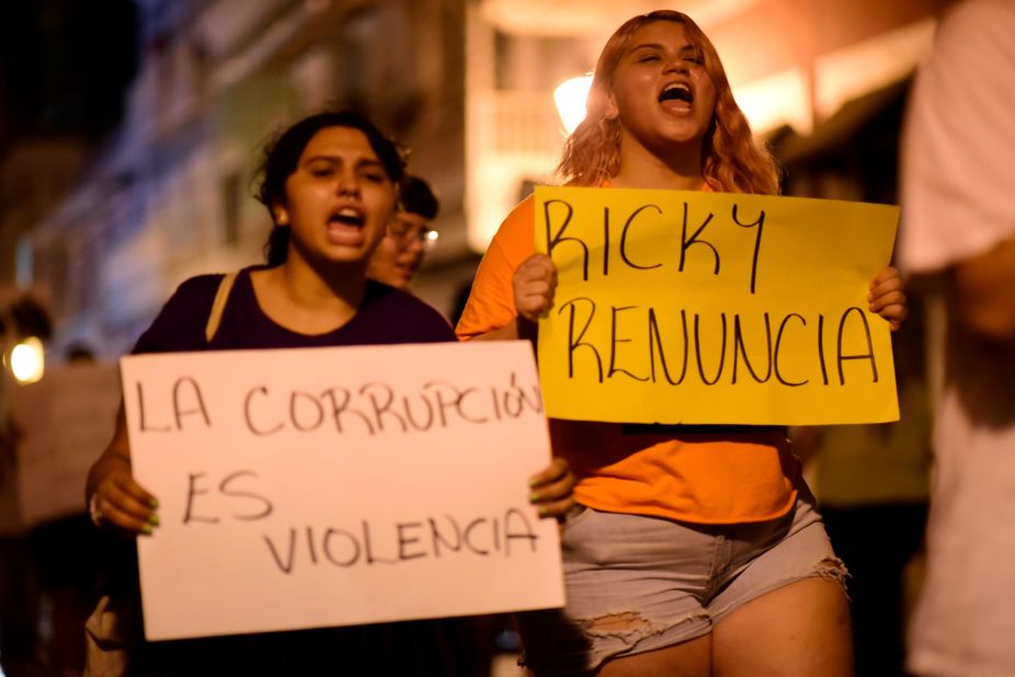 Demonstrators hold signs that say "Corruption is violence" and "Ricky resign" while protesting near the executive mansion on Thursday, July 11.