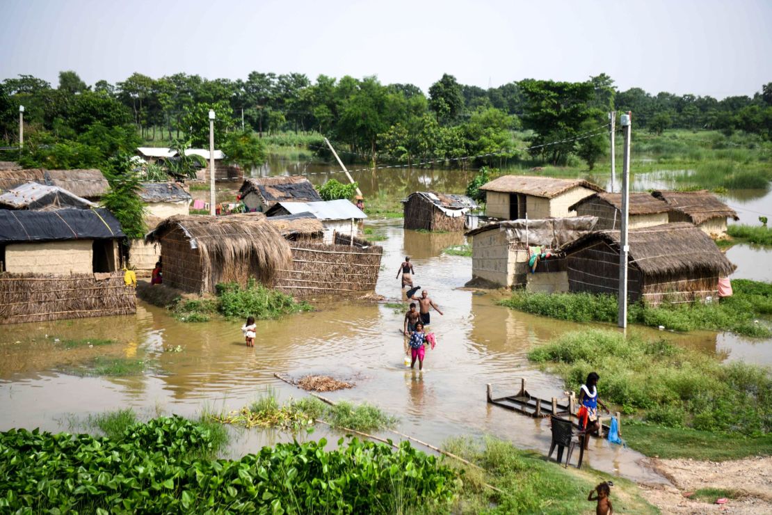 Indian residents in Bihar state wade through a flooded village on July 17, 2019. 