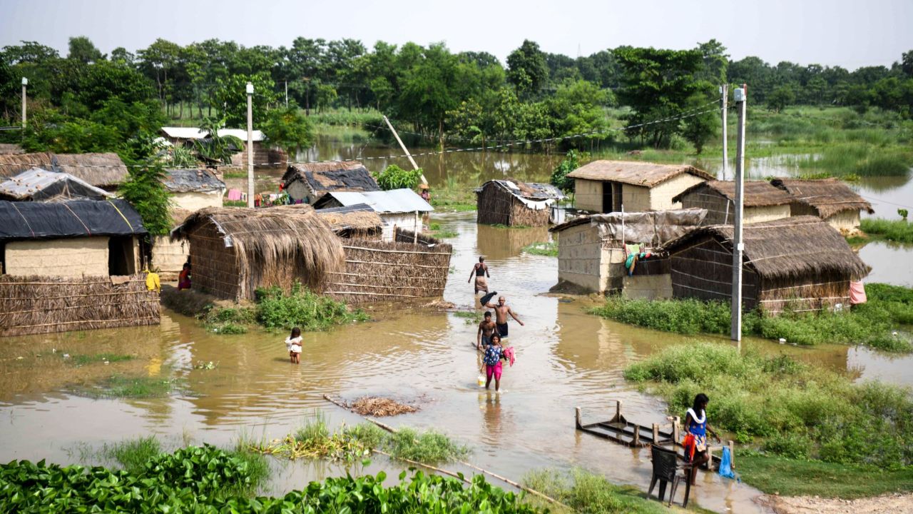 Indian residents in Bihar state wade through a flooded village on July 17, 2019. 