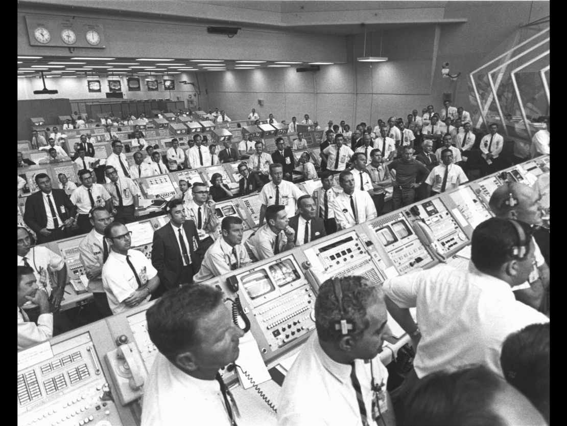 Members of the Kennedy Space Center government-industry team rise from their consoles within the Launch Control Center to watch the Apollo 11 liftoff through a window.
