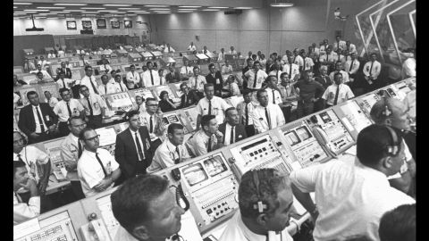 Members of the Kennedy Space Center government-industry team rise from their consoles within the Launch Control Center to watch the Apollo 11 liftoff through a window. 