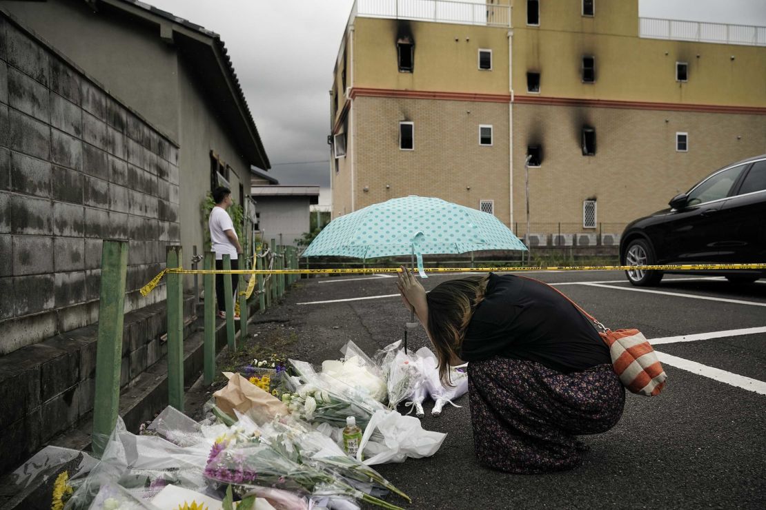 A woman prays next to flowers and tributes laid at the scene of the Kyoto Animation fire.
