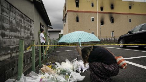 A woman prays next to flowers and tributes laid at the scene of the Kyoto Animation fire.
