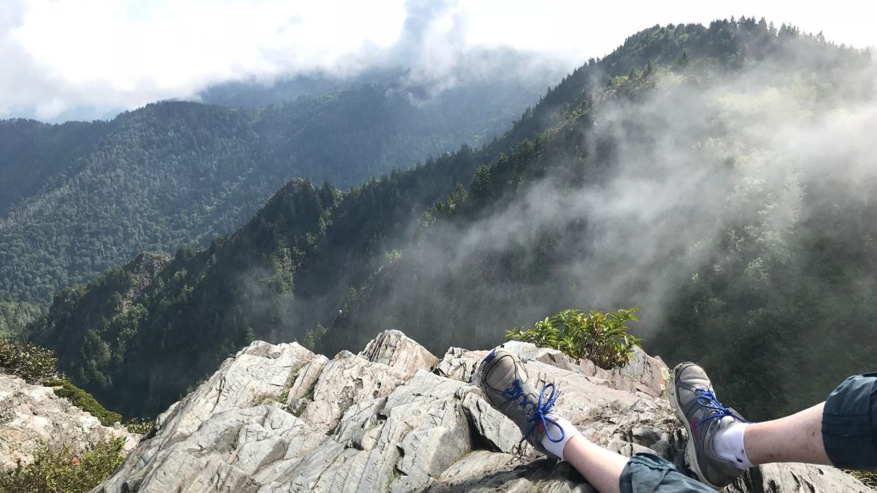 A hiker takes a deserving rest and soaks in the view on the Charlies Bunion Hiking Trail. Drifting patches of clouds are a frequent and enchanting part of the park experience.