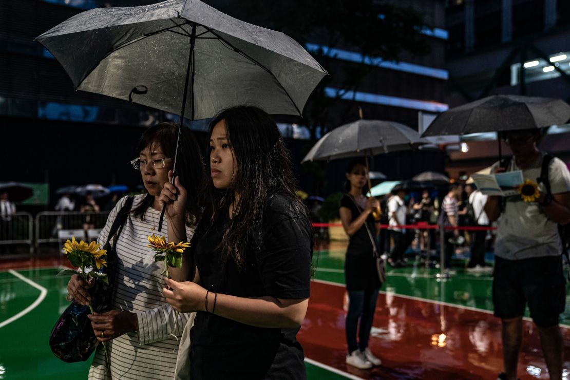 People hold flowers in the rain ahead of a memorial service on July 11, 2019, in Hong Kong, for a protester who died.