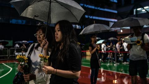 People hold flowers in the rain ahead of a memorial service on July 11, 2019, in Hong Kong, for a protester who died.