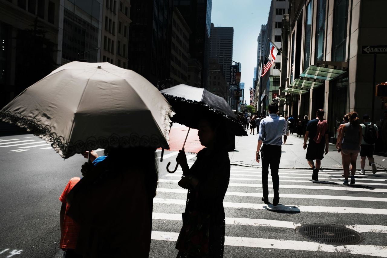 People hold umbrellas to shade themselves from the sun on July 19, in New York.