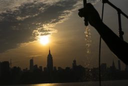 The sun rises over New York City and the Empire State Building while a man sprays water at Pier A.